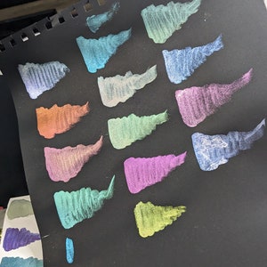 Pu&ograve; includere: Un foglio di carta nero con 13 campioni di vernice metallizzata in vari colori, tra cui turchese, verde, viola e oro.