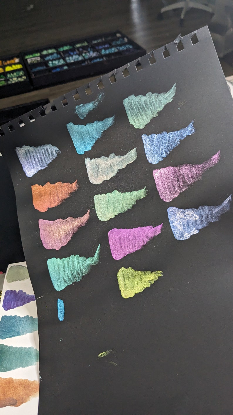 Pu&ograve; includere: Un foglio di carta nero con 13 campioni di vernice metallizzata in vari colori, tra cui turchese, verde, viola e oro.