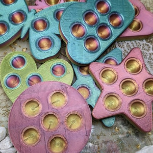May include: A collection of colourful, iridescent, silicone fidget toys in the shapes of a butterfly, cloud, heart, star, and circle. Each toy has multiple dimples that can be pushed in and out.
