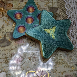 May include: Two teal star-shaped fidget toys. One star has a pop-it design with six circles. The other star has a yellow butterfly design.