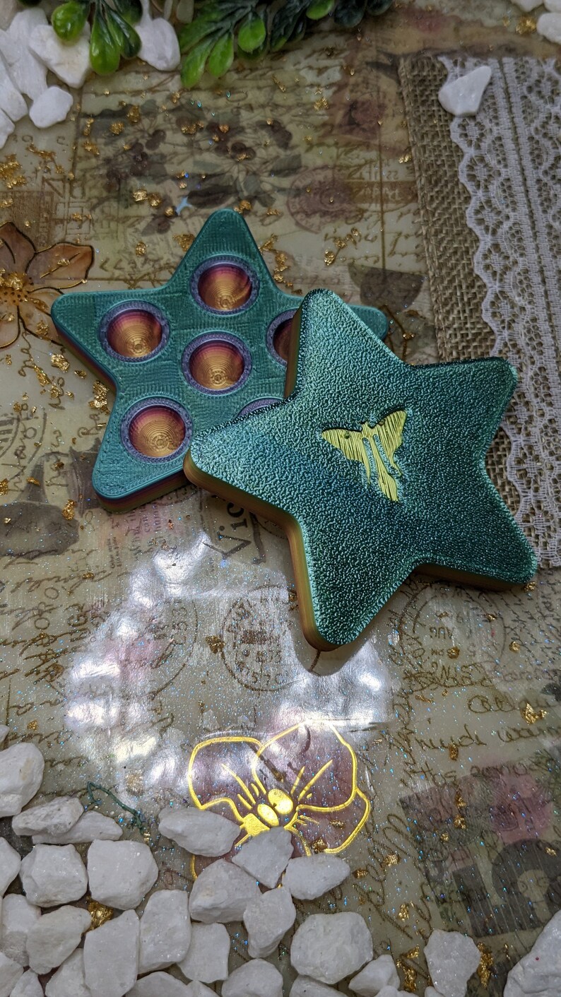 May include: Two teal star-shaped fidget toys. One star has a pop-it design with six circles. The other star has a yellow butterfly design.