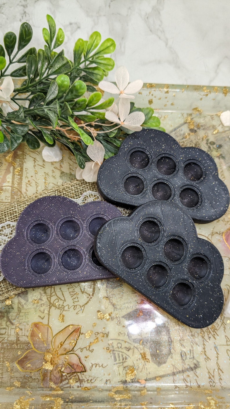 May include: Two black cloud-shaped silicone fidget toys with a sparkly finish. Each toy has six round dimples that can be pushed in and out.