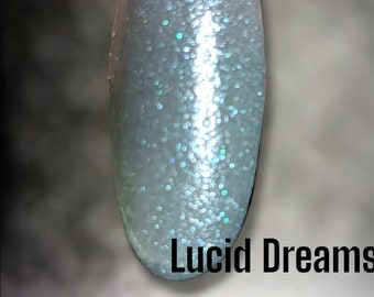 Może przedstawiać: Przezroczysty, opalizujący brokatowy puder do zanurzania z białą bazą. Puder nazywa się "Lucid Dreams" i jest częścią marki "Bloom Dip".