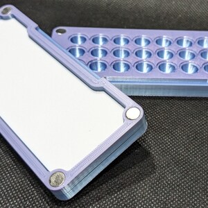 May include: A purple 3D printed box with a lid. The lid has 24 round holes. The box is made of plastic and has a smooth finish.
