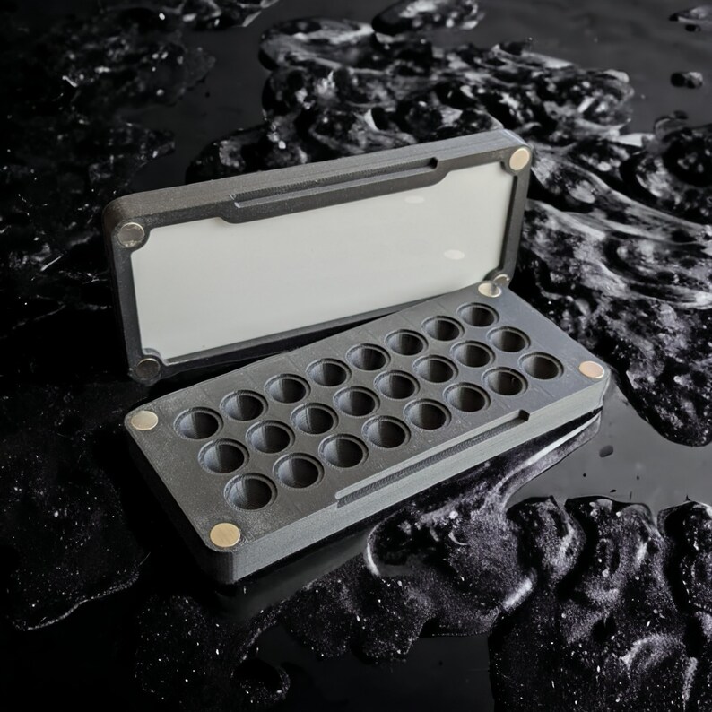 May include: A black plastic case with a hinged lid and 25 round compartments. The case is open and the compartments are visible.