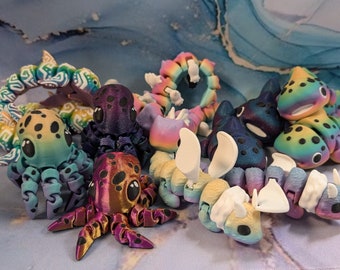 May include: A collection of colorful, handmade octopus and sea creature figurines. The octopus figurines are made with a variety of colors, including purple, green, and orange. The sea creatures are made with a variety of colors, including blue, green, and yellow.