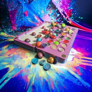 May include: A pink and white makeup palette with a variety of colourful eyeshadows. The palette is open and some of the eyeshadows are missing. The eyeshadows are scattered around the palette on a colourful background.