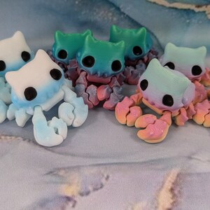 Pode incluir: Uma cole&ccedil;&atilde;o de seis pequenas estatuetas de caranguejo de cer&acirc;mica pintadas &agrave; m&atilde;o e coloridas. Os caranguejos s&atilde;o pintados em tons de azul, verde, rosa e branco. Cada caranguejo tem um design &uacute;nico e apresenta um rosto bonito e de estilo de desenho animado.