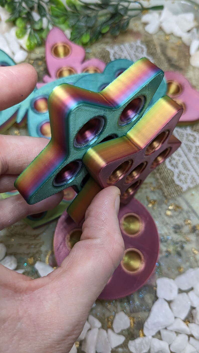 May include: A set of three iridescent fidget toys in the shape of a star, butterfly, and circle. The toys are made of a smooth, colourful plastic and have a variety of textures.
