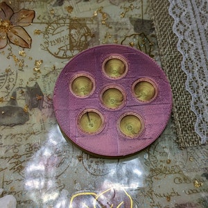 May include: A round, pink, 3D printed tray with six circular indentations. The indentations are gold in colour and have a concentric circle design.