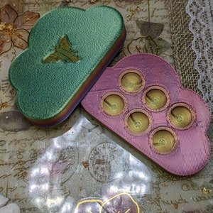 May include: Two cloud-shaped resin trays. One is green with a butterfly design and the other is pink with six circular indentations.