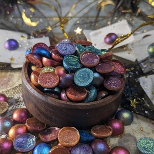 Pu&ograve; includere: Una ciotola di legno piena di cabochon rotondi, piatti e iridescenti di vari colori. La ciotola &egrave; circondata da altri cabochon in varie tonalit&agrave; di blu, verde, viola e arancione.