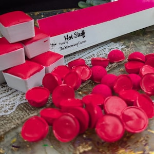 May include: A set of 9 red watercolor paint pans in white pans, stacked in a pyramid shape.  The paint pans are labeled "Hot Stuff" and "Painted by The Blooming Faerie".  There are also 20 loose red watercolor paint rounds.