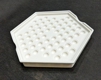 Pode incluir: Bandeja hexagonal branca com uma grade de reentrâncias redondas. A bandeja é feita de plástico e tem uma superfície lisa.