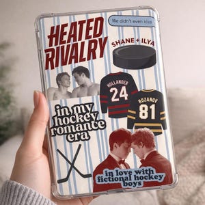 May include: Transparent phone case with a design featuring the text "HEATED RIVALRY" and "in my hockey romance era." Includes images of hockey jerseys, a puck, and two pairs of men. Text includes "SHANE + ILYA," "HOLLANDER 24," and "ROZANOV 81."