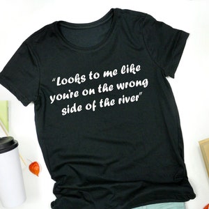 May include: Black t-shirt with white text that reads "Looks to me like you're on the wrong side of the river"