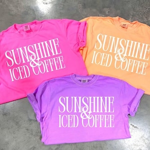 May include: Three t-shirts with the text "Sunshine & Iced Coffee" in white lettering on a pink, orange, and purple background.