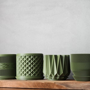 May include: Four green ceramic planters with different geometric patterns. The planters are arranged in a row on a wooden surface.