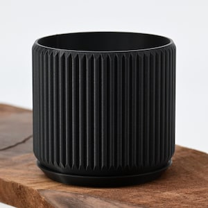 May include: A black plastic planter with a ribbed design. The planter has a matching saucer.