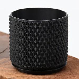 May include: A black plastic planter with a geometric pattern. The planter has a removable base.