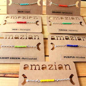 May include: Six different color bracelets on display cards with the word "amazian" printed on each card. The bracelets are made of silver chains with colored beads. The cards also include the color of the bracelet and a word describing the color. The colors are blue, orange, red, green, light green, and purple.