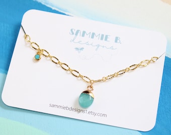Könnte beinhalten: Eine goldene Kettenkette mit einem Anhänger aus türkisfarbenem Edelstein und einem kleineren türkisfarbenen Edelstein-Anhänger. Die Kette wird auf einer weißen Karte mit dem Text "SAMMIE B. designs" und einer Website-Adresse präsentiert.