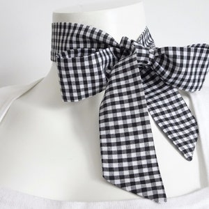 May include: A black and white gingham bow tie. The bow tie is tied around a white mannequin's neck.