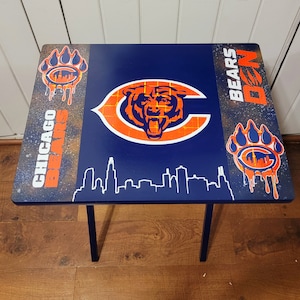 May include: A blue folding table with a Chicago Bears logo and the words "Chicago Bears" and "Da Bears" printed on it. The table has a bear paw print on each side.