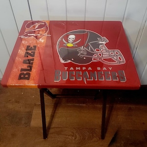 May include: A red folding table with a Tampa Bay Buccaneers logo and the words "Blaze" and "Tampa Bay Buccaneers".