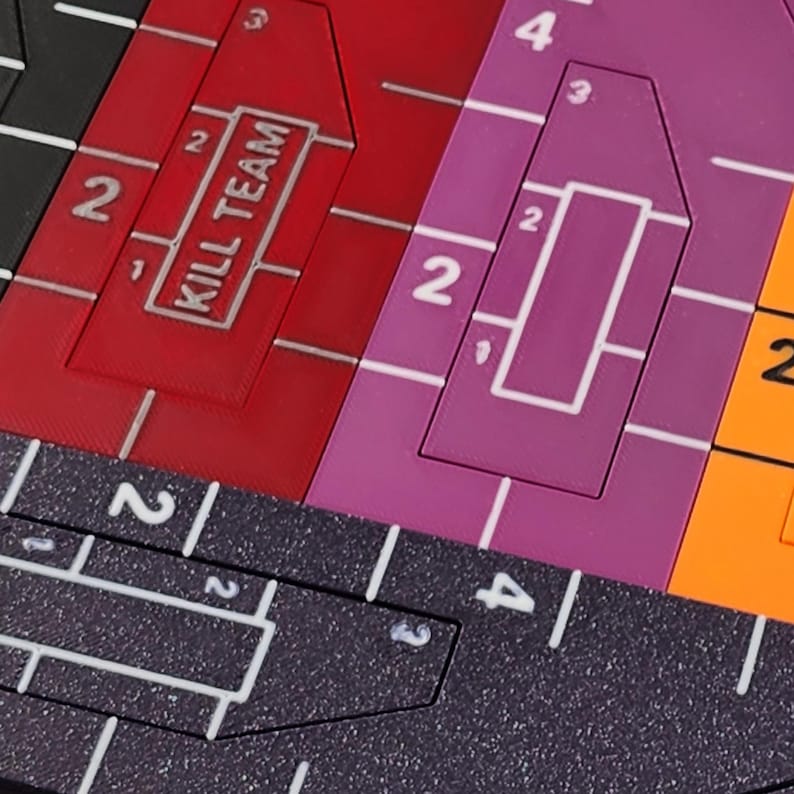 Op de afbeelding: Close-up van een kleurrijk spelbord met geometrische vormen en cijfers. Het bord heeft rode, paarse en oranje secties met witte rasterlijnen en de tekst "KILL TEAM".