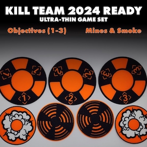 May include: A game set with the text "KILL TEAM 2024 READY" and "ULTRA-THIN GAME SET". The set includes black and orange objective markers numbered 1-3, and mine and smoke markers. The objective markers are circular with orange centers.