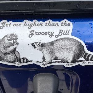 May include: A white sticker with a black and white illustration of two raccoons. The sticker says "Get me higher than the grocery bill" and is signed "Tyler Childers".