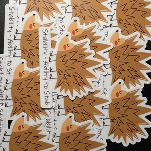 Könnte beinhalten: Mehrere braune und weiße Igel-Aufkleber mit dem Text "Stability - Ability to Stab", der auf jedem Aufkleber wiederholt wird.