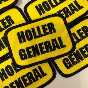 May include: Close-up of several yellow fabric patches with black stitching. The patches have the text "HOLLER GENERAL" printed on them.
