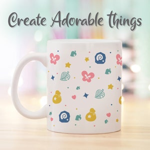 May include: White ceramic mug with a pattern of pink flowers, yellow stars, green leaves, blue and white shells, and yellow money bags. The text "Create Adorable Things" is written in gray at the top of the mug.