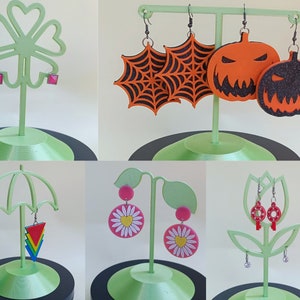 May include: Assortment of earring displays featuring various styles of earrings. The displays are made of green plastic and feature a variety of shapes, including a clover, an umbrella, a flower, and a pumpkin. The earrings are made of different materials, including metal, plastic, and wood. The earrings are in a variety of colors, including pink, red, orange, yellow, green, blue, and black.