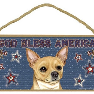 May include: A wooden sign with a blue background and white stars. The sign says "God Bless America" in red, white, and blue letters. A tan chihuahua with brown eyes is in the center of the sign.