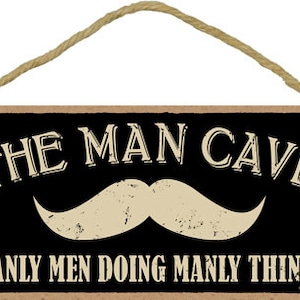 May include: A black and white wooden sign with the text "The Man Cave Manly Men Doing Manly Things" and a white mustache graphic.