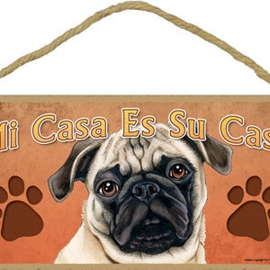 Puede incluir: Un letrero de madera con el texto "Mi Casa Es Su Casa" en letras naranja y marrón. Un lindo perro pug con ojos marrones y nariz negra se presenta en el centro del letrero. Dos huellas de patas marrones están a cada lado del perro.