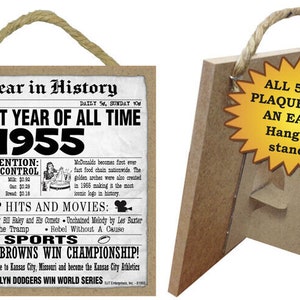 May include: A brown wooden plaque with a newspaper-style design featuring the year 1955 and the text "The Best Year of All Time". The plaque includes a list of events, top hits, and movies from 1955. The plaque has a rope hanger and a stand.