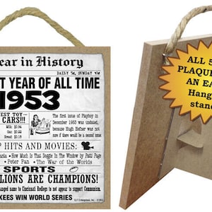 May include: A brown wooden plaque with a newspaper-style design featuring the year 1953 and the text "The Best Year of All Time". The plaque has a rope hanger and a stand for displaying on a table or shelf. The plaque measures 5 inches by 5 inches.