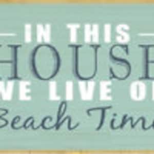 May include: A teal blue wooden sign with white text that reads "In this house we live on beach time".