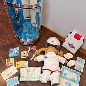 May include: A vintage Cabbage Patch Kids Astronauts doll set. The set includes a doll in a white spacesuit, a helmet, adoption papers, and other accessories. The packaging is a blue and silver box with the words "Young Astronauts" on it.