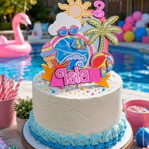 May include: A two-tiered cake with white frosting and blue wave-like frosting at the bottom. The cake is decorated with a colorful topper featuring a sun, sunglasses, palm tree, and the name "Isla".