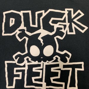 May include: Black t-shirt with a white graphic of a skull with the words "Duck Feet" printed below.