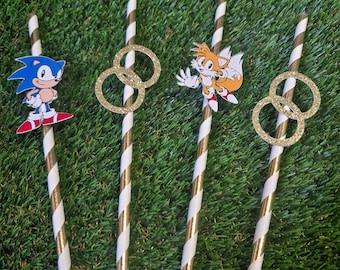 May include: Four drinking straws with white and metallic gold diagonal stripes. Two straws feature a cutout of the blue hedgehog character Sonic or the orange fox character Tails. Two straws feature a pair of interlocking gold glitter rings.