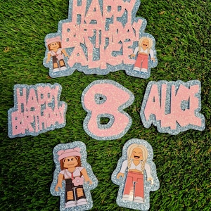 May include: Pink and blue glitter cake toppers with the words "Happy Birthday Alice" and the number "8". There are also two images of Roblox characters.