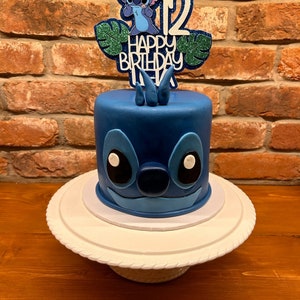 K&ouml;nnte beinhalten: Ein blauer Geburtstagskuchen mit einem Stitch-Design. Der Kuchen hat einen Aufsatz mit der Zahl 12, Stitch und den Worten "Happy Birthday Alex". Der Kuchen steht auf einer wei&szlig;en Tortenplatte.
