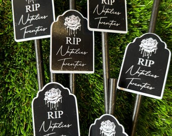 May include: A set of black straw toppers shaped like tombstones, each featuring a white graphic of a dripping rose, the text RIP, and the script text Natalies Twenties. The toppers are attached to thin black straws for use in beverages.