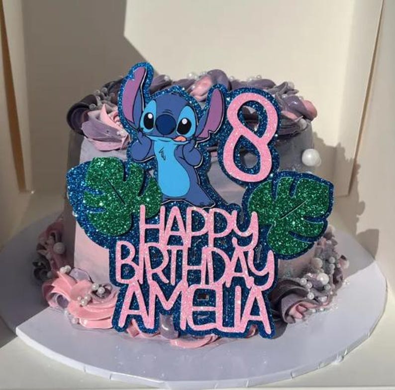 K&ouml;nnte beinhalten: Ein dekorierter Kuchen mit einem Stitch-Charakter als Tortenaufsatz. Der Kuchen hat rosa und graue Glasur mit dekorativen Elementen. Der Aufsatz tr&auml;gt die Aufschrift "Happy Birthday Amelia" und die Zahl "8".